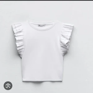 Vit topp med volangärmar från Zara - Säljer en söt vit topp från Zara med volangdetaljer på ärmarna. Perfekt för en stilren och chic look. Toppen är kortärmad och har en rund halsringning. I stlrk s