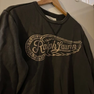 Sweatshirt från Ralph Lauren - Snygg mörkgrön sweatshirt från Ralph Lauren med ett stort tryck på framsidan. Tröjan har långa ärmar och en rund halsringning. Perfekt för en avslappnad stil. Väl använd men fortfarande okej skick.