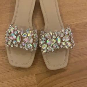 Beige sandaler med glittriga detaljer - Eleganta beige sandaler med fyrkantig tå och glittriga stenar på ovandelen. Perfekta för att ge en touch av glamour till din outfit.