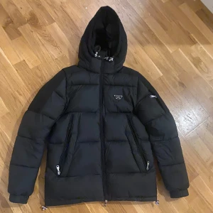 Svart dunjacka från Alessandro - Helt ny Snygg svart dunjacka från Alessandro med huva och dragkedja. Jackan har långa ärmar och flera praktiska fickor med dragkedjor. Perfekt för kyliga dagar. Storlek S men passar M också!