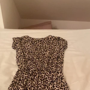 Leopardmönstrad klänning från Lindex - Snygg leopardmönstrad klänning från Lindex med korta ärmar och dragkedja i ryggen. Perfekt för att sticka ut med ett djärvt mönster. Tillverkad i ett mjukt och bekvämt material.