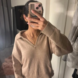 Beige stickad tröja från Dilvin Knit - Säljer en snygg beige stickad tröja från Dilvin knit. Tröjan har en v-ringad design med krage och långa ärmar. Perfekt för en stilren och bekväm look.