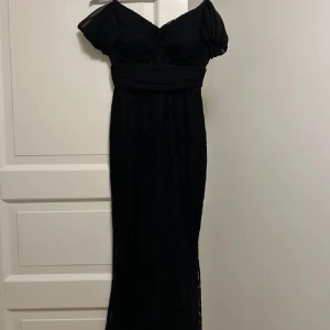 Svart långklänning med kortärmad design - Elegant svart långklänning med kortärmad design och v-ringad hals. Perfekt för en stilfull kväll med en klassisk look.