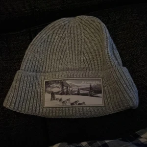 Grå ribbad mössa med patch.  - Snygg grå ribbad mössa med en cool patch framtill som ger en unik stil. Perfekt för kyliga dagar.. aldrig andvänd 