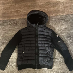 Moncler Cardigan - Snygg svart jacka från Moncler med quiltad design och ribbade detaljer. Jackan har en huva och dragkedja framtill. Perfekt för kyligare dagar. Storlek 3 vilket motsvarar M/L, skulle rekommendera dig som bär M. (Kvitto samt annat bevismaterial kan visas vid behov)