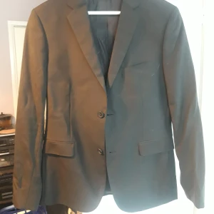 Svart kavaj från Bläck - Snygg svart kavaj från Bläck med skräddarsydd passform. Kavajen har två knappar framtill och fyra dekorativa knappar vid ärmsluten. Perfekt för en stilren look.