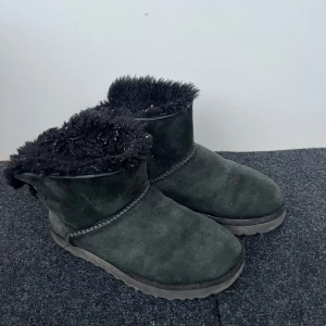 Svarta boots från UGG - Mysiga svarta boots från UGG med fluffigt foder och rosett baktill. Perfekta för kalla dagar när du vill hålla fötterna varma och bekväma. Välanvända, sulan inuti är lite sliten men annars är de i bra skick och har mer att ge😇💓