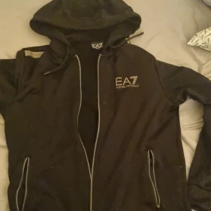 Ea7 hoodie - Snygg svart hoodie från EA7 Emporio Armani med dragkedja och huva. Perfekt för en casual look. Märkeslogga på bröstet och praktiska fickor framtill.