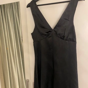 Svart klänning med v-ringning - Elegant svart klänning med djup v-ringning och ärmlös design. Perfekt för en stilren look. Pris går att diskuteras, aldrig använd.