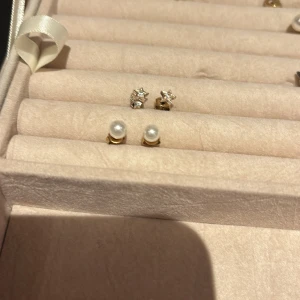Bundel örhängen  - Två par örhängen, ett med vita pärlor och ett med stjärnformade detaljer i guld. Perfekta för att ge en elegant touch till din stil.