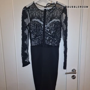 Svart spetsklänning från Bubbleroom - Elegant svart klänning från Bubbleroom med vacker spetsdetaljering och långärmad design. Klänningen har en figurnära passform och en dragkedja i ryggen för enkel påklädning. Perfekt för en stilfull kväll. Den har även prislappen kvar!