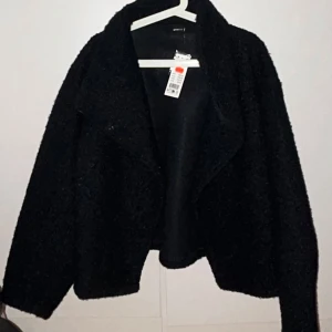 Mörkblå teddyjacka - Mysig svart teddyjacka från Gina med lång ärm och en stilren design. Perfekt för kyliga dagar när du vill hålla dig varm och trendig. Jackan har en enkel och elegant look som passar till många olika outfits.