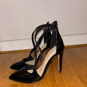 Svarta pumps med remmar - Eleganta svarta pumps med hög klack och spetsig tå. Skorna har smala remmar som korsar över foten och en justerbar ankelrem för extra stöd.  Säljer pågrund av att dom är för små för mig 