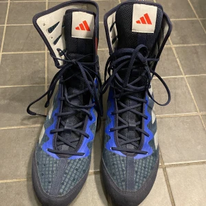 Adidas boxningsskor med blå och vita detaljer nya -  Original pris 1200 men säljer dem för 900 Snygga Adidas boxningsskor i mörkblått med vita och blå detaljer. Skorna har hög snörning och en röd Adidas-logga på plösen. Perfekta för boxningsträning med en stilren design och bra stöd.