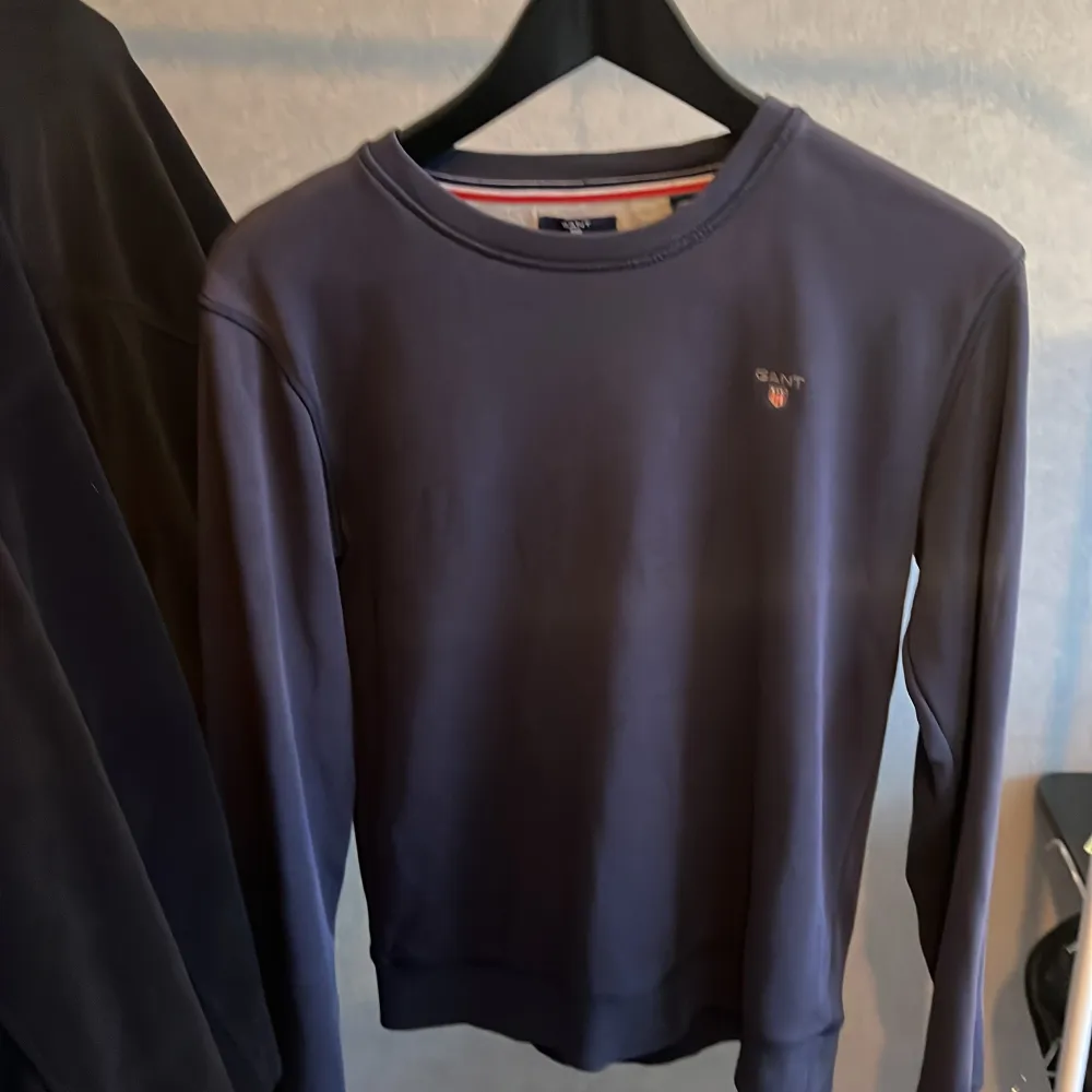Säljer en stilren mörkblå tröja från Gant med rund halsringning. Tröjan har en liten logotyp broderad på bröstet och är perfekt för en avslappnad look. Passar bra till både jeans och chinos.. Neuletakit & Villapaidat.