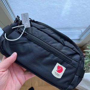 Fjällräven axelväska high coast - Helt ny svart axelväska i modellen high coast från Fjällräven med flera fack och dragkedja. Fick väskan i present men kommer ej till användning. Väskan har en justerbar rem och är tillverkad i slitstarkt material