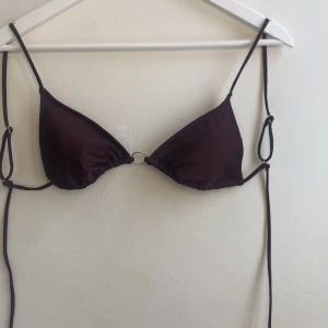 Brun bikiniöverdel med knytband - Snygg brun bikiniöverdel med justerbara knytband och guldringdetalj framtill. Perfekt för en dag på stranden eller vid poolen. Enkel och stilren design som passar till det mesta.