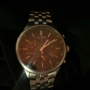Citizen Eco-Drive herrklocka - Stilren Citizen Eco-Drive herrklocka med silverfärgad länkarmband och mörk urtavla. Klockan har datumvisning och flera små urtavlor för extra funktioner. Perfekt för den som söker en kombination av elegans och funktionalitet. Klockan har ett värde på 3000kr 