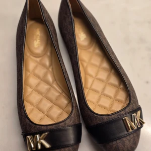 Bruna ballerinaskor från Michael Kors - Helt nya stilrena bruna ballerinaskor från Michael Kors med quiltad insida och guldfärgade MK-detaljer framtill. Perfekta för en elegant och bekväm look. Endast provade!