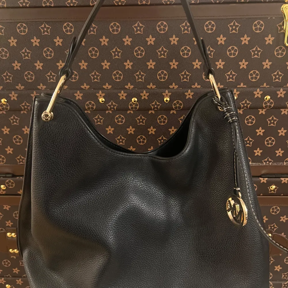 Elegant svart axelväska i skinn från Michael Kors med guldfärgade detaljer och logotyp. Väskan har en rymlig insida och en praktisk axelrem. Perfekt för att bära dina dagliga nödvändigheter med stil. Väldigt bra pris för en sån fin väska, väldigt bra kvalité på den. . Laukut & Käsilaukut.