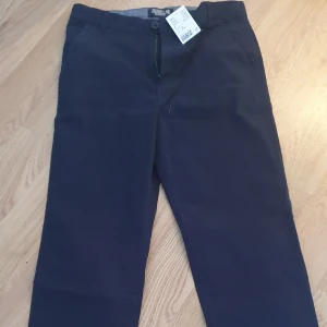 Mörkblå slim fit byxor från ORGNLS, chinos - Snygga mörkblå slim fit byxor från ORGNLS med dragkedja och knappstängning. Chinos. Perfekta för en stilren look. Passar ungdomar i storlek 164.
