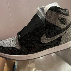 Nike Air Jordan 1 Retro High OG - Snygga Nike Air Jordan 1 Retro High OG i svart och grått med unikt mönster och textdetaljer. Skorna har en hög siluett och klassisk snörning. Perfekta för sneaker-entusiaster som vill sticka ut.nya fast trasig låda