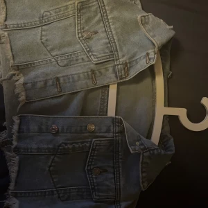 Blå jeansjacka med slitna detaljer - Säljer en cool jeansjacka med slitna detaljer och fransar. Perfekta för en avslappnad stil. Den har klassiska fickor och knappar framtill. Helt ny aldrig använd, nypris 200kr