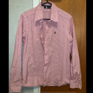 Röd och vit rutig skjorta från Sail Racing - Snygg röd och vit rutig skjorta från Sail Racing i herrstorlek M. Skjortan har långa ärmar och klassisk krage med knappar framtill. Den är i mycket bra skick och endast använd vid ett par tillfällen.