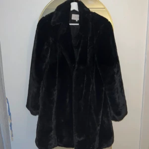 Svart pälsjacka - Snygg och elegant svart pälsjacka med lång ärm och klassisk design. Perfekt för att hålla sig varm och stilren under kyliga dagar. Jackan har en mjuk och lyxig känsla.