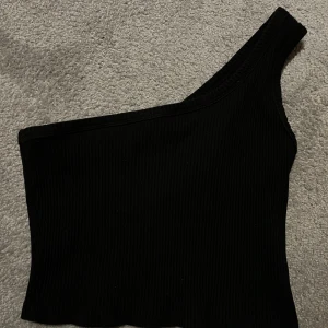 Svart oneshoulder topp från Shein - Snygg svart oneshoulder topp från Shein i ribbat material. Perfekt för en stilren look med en unik asymmetrisk design. Passar bra till både jeans och kjol.