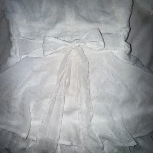 Klänning - Vit klänning med osynlig dragkedja i bak. Rosetten går att knyta upp och göra sin egna " knut" fram och bak. Klänning med en byxdress under som inte alls syns. Använd en gång och har inga defekter. Köpt från new yorker för 350kr. Midjan justerbar 