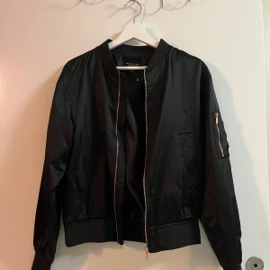 Svart bomberjacka från The Black Label Collection - Säljer en snygg svart bomberjacka från The Black Label Collection i storlek XS. Jackan har en  dragkedja i kopparfärg och en ficka på ärmen. Perfekt för höst och vår! 🖤Aldrig använd! 