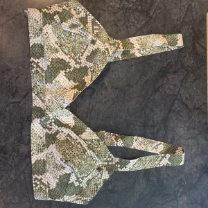 Grön och vit bikini från H&M - Snygg bikiniöverdel från H&M i grönt och vitt ormmönster. Den har justerbara axelband och en bekväm passform. Perfekt för sommarens stranddagar eller poolhäng. Materialet känns mjukt och skönt mot huden. 🐍 är helt nya, enbart testad