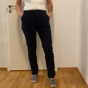 Svarta byxor  - Säljer ett par svarta byxor i storlek 36. De är tillverkade i en skön polyesterblandning med elastan för extra stretch. Byxorna har en hög midja och en slim passform, perfekt för både vardag och fest. De har en enkel design med knapp och dragkedja framtill.