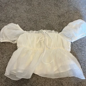 Vit offshoulder blus - Säljer en superfin vit offshoulder blus med puffiga ärmar. Den har en luftig och lätt design, perfekt för sommardagar. Blusen är i ett tunt och skönt material med en söt knytning i midjan. Passar perfekt till både jeans och kjol!