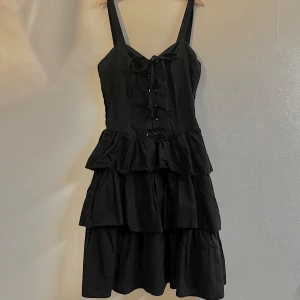 Kort volang klänning  - Klänningen är knappt använd och bra skick men köpt secondhand. Lite trasig vid öljetterna(metall ringarna som bandet träs igenom), syns bäst på bild tre. Längden på axelbanden går att justera. Skulle säga storlek M. Köpare står för frakt 😽