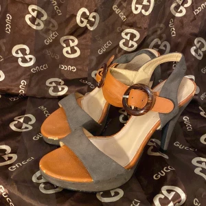 Marie Claire klackskor med spänne - Snygga klackskor från Marie Claire i en mix av orange och brunt. De har en elegant design med ett stort spänne på sidan och en bekväm klack. Perfekta för en utekväll eller fest. Skorna är i bra skick och redo att användas!