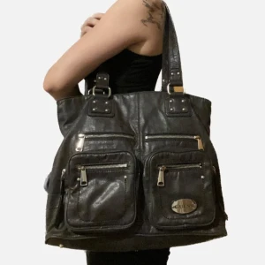 Snygg vintage axelväska Guess - Så snygg svart shoulderbag från Guess i skinn. Den är köpt i vintage butik i USA men är aldrig använd av mig så den är i bra skick. Den har mycket utrymme och massa coola fickor. Skriv om du har några frågor :)
