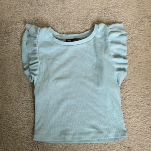 Ljusblå topp från Zara - Säljer en söt ljusblå topp från Zara i storlek S. Den har volangdetaljer på ärmarna och är gjord i ett ribbat material. Perfekt för vår och sommar! 💙