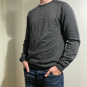 Grå stickad tröja - Säljer en stilren grå långärmad tröja i mjukt material. Perfekt för både vardag och lite kyligare dagar. Tröjan har en normal passform och är superbekväm att ha på sig. Passar bra till jeans eller chinos för en avslappnad look.