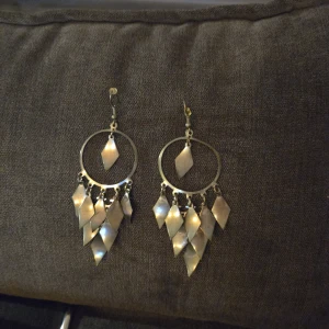 Silvriga örhängen med hängande detaljer - Snygga silvriga örhängen med en cirkulär design och flera hängande diamantformade detaljer. Perfekta för att ge en glittrig touch till din outfit. Passar både till vardags och festliga tillfällen.