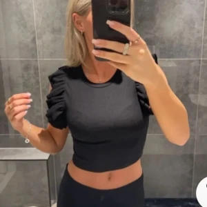 Svart croppad topp med volangärmar - Säljer en snygg svart croppad topp med volangdetaljer på ärmarna. Perfekt för en utekväll eller fest! Toppen är tight och framhäver figuren på ett stilrent sätt. Passar bra till både jeans och kjol.