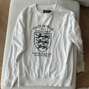 Vit sweatshirt från Morris - Säljer en stilren vit sweatshirt från Morris med ett coolt tryck på framsidan. Tröjan är i bomull och har långa ärmar. Perfekt för en avslappnad stil eller för att hålla sig varm under kyligare dagar. Passar både till vardags och lite mer uppklädda tillfällen.