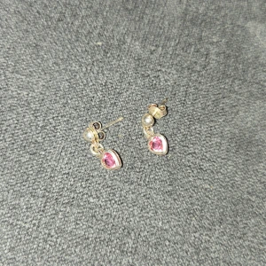 Silverörhöngen med rosa hjärtan - Säljer ett par söta örhängen i äkta silver med rosa hjärtformade stenar. Perfekta för att ge en romantisk touch till din outfit. De är små och diskreta, men ändå iögonfallande med sina glittrande rosa detaljer. Passar både till vardags och festliga tillfällen. 💖