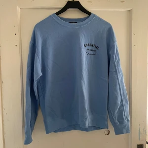 Blå sweatshirt från Essentials - Säljer en snygg ljusblå sweatshirt från Essentials. Den har en avslappnad passform och är perfekt för både vardag och chill. Tröjan har långa ärmar och en rund halsringning. Texten 'Essential Collection' är tryckt på bröstet. Perfekt för höst och vår!