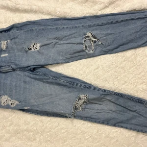 Blå ripped jeans - Säljer ett par blå ripped jeans från New Yorker i storlek M. De har en cool, sliten look med flera hål och slitningar på framsidan och baksidan. Perfekta för en avslappnad och trendig stil. Passar bra till både vardag och fest!