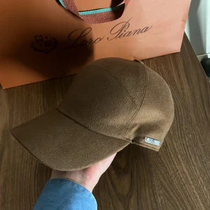 Loro Piana keps - Snygg brun keps från Loro Piana i baby kashmir. Kepsen har en elegant design med en liten metallplatta på sidan. Perfekt för en stilren look. 6,900kr ny