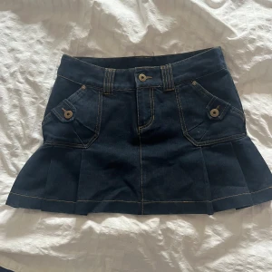 Mörkblå jeanskjol med volang - Superfin vintage mörkblå jeanskjol från Vero Moda med volanger. I midjan är kjolen 38,5cm (mätt platt) och med volangdelen inräknad 33cm lång. 