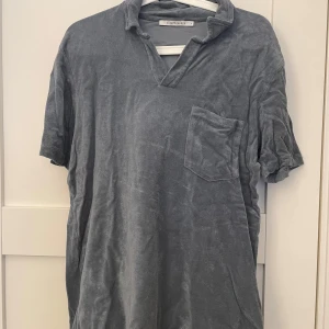 Blå/grå frotté pike från A Days March - Säljer en stilren grå kortärmad t-shirt från A days March. T-shirten har en avslappnad passform med en bröstficka och en v-ringad krage. Perfekt för en casual look.