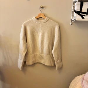 Beige stickad tröja från Zara - En såååå snygg och trendig stickad tröja från Zara i storlek XS. Den är varm, mysig och i väldigt bra skick. Tröjan har vita linjer fram och baktill samt slitsar i slutet vid midjan (skriv för bild). 🩷🩷 Hör av er om ni undrar något.